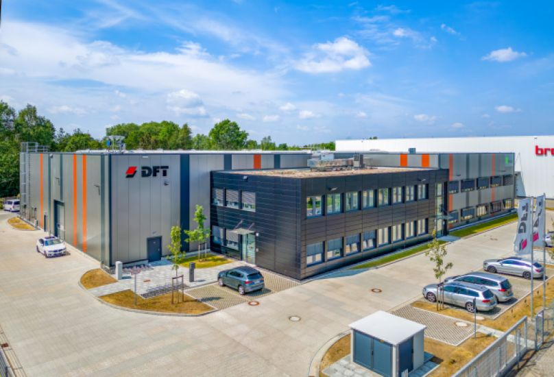 Photo of the warehouse "Hansalinie Bremen - Jacob Flooring". Pictured is a large warehouse with the inscription "DFT". In front of it is a black office building with a glazed entrance door.