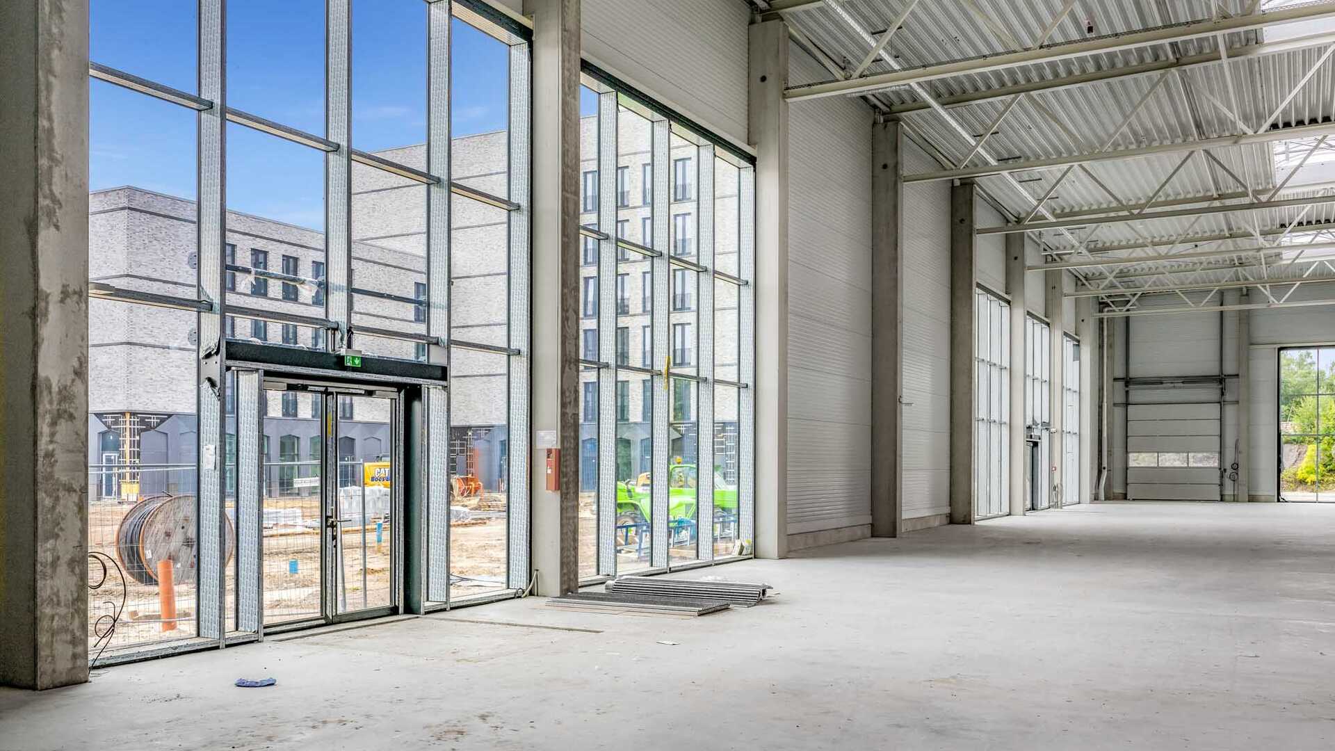 Foto aus der Bauphase des Spurwerkkomplexes. Dargestellt ist eine große Halle mit Glasfront als Eingang und hohen Decken. Außerhalb der Halle sind Baugeräte und weitere Gebäude des Spurwerkkomplexes zu sehen.